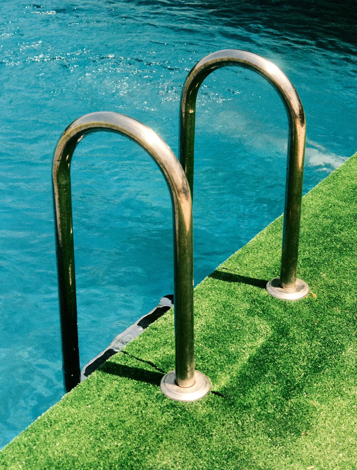 Artificial grass beside a backyard pool with a steel ladder